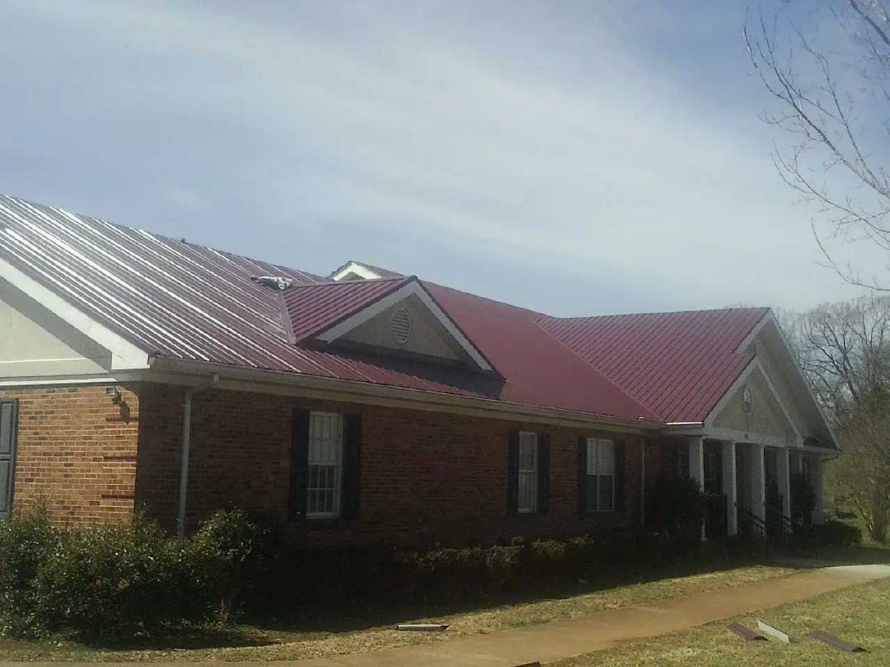 Red metal roof with gabled entries on a long brick building, from a Hail Damage Roof Repair job in Roseville