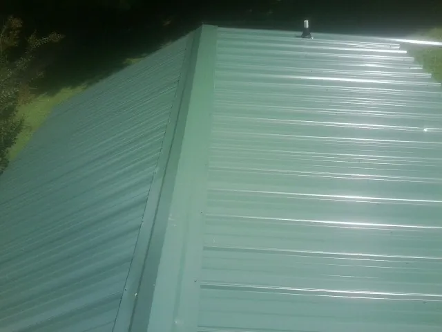 New green metal panels meeting at the ridge of a roof — Flat Roof Repair work by our crew in Roseville