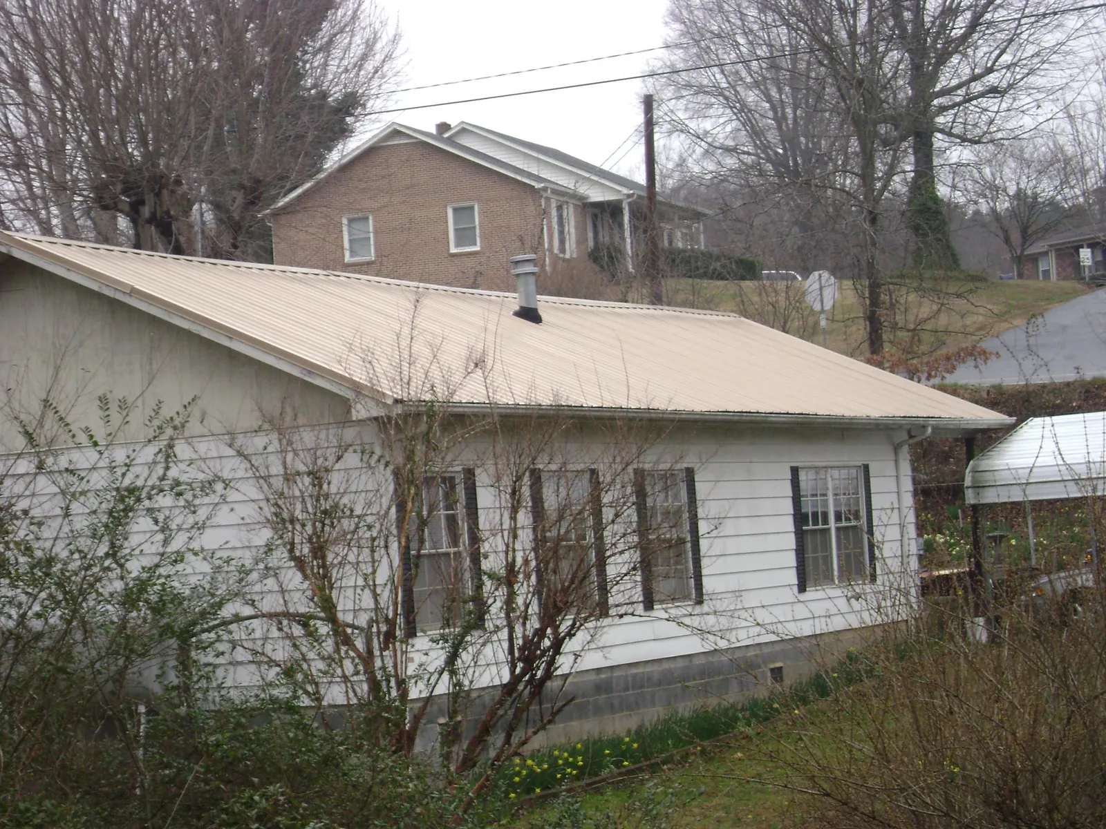 Tan metal roof on a white sided house set into a hillside — Commercial Roofing by Roofing Brothers in Roseville